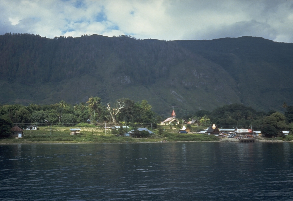 The steep wall behind Tomok village on Samosir Island is part of a block of uplifted caldera-fill rocks. The entire 630 km2 island, which now rises to 700 m above Lake Toba, is capped with lake-floor sediments that were deposited before the island was uplifted above lake level. Photo by Tom Casadevall, 1987 (U.S. Geological Survey)