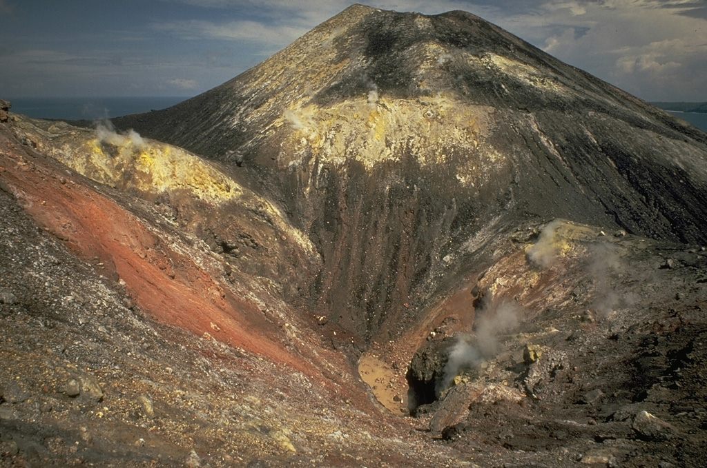 Steam rises from a fissure cutting the summit cone of Anak Krakatau in 1979.  Broad areas of hydrothermal alteration color the crater walls.  Frequent explosive activity since 1927, sometimes accompanied by lava flows, has constructed an island 2 km in diameter, with a height of about 300 m. Copyrighted photo by Katia and Maurice Krafft, 1971.