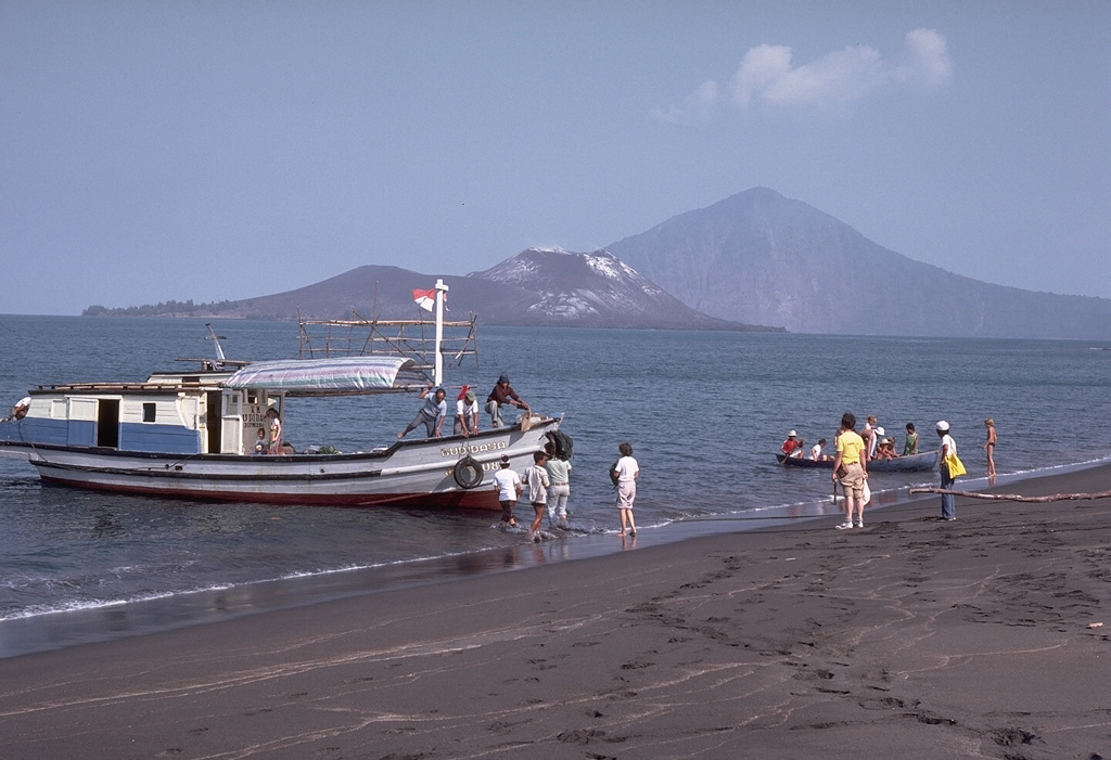 A boatload of visitors prepares to sail to Anak Krakatau Island, seen behind the boat. Anak Krakatau was constructed within the 1883 caldera, whose southern rim forms Rakata peak in the background to the right. Photo by Dick Fiske, 1983 (Smithsonian Institution).