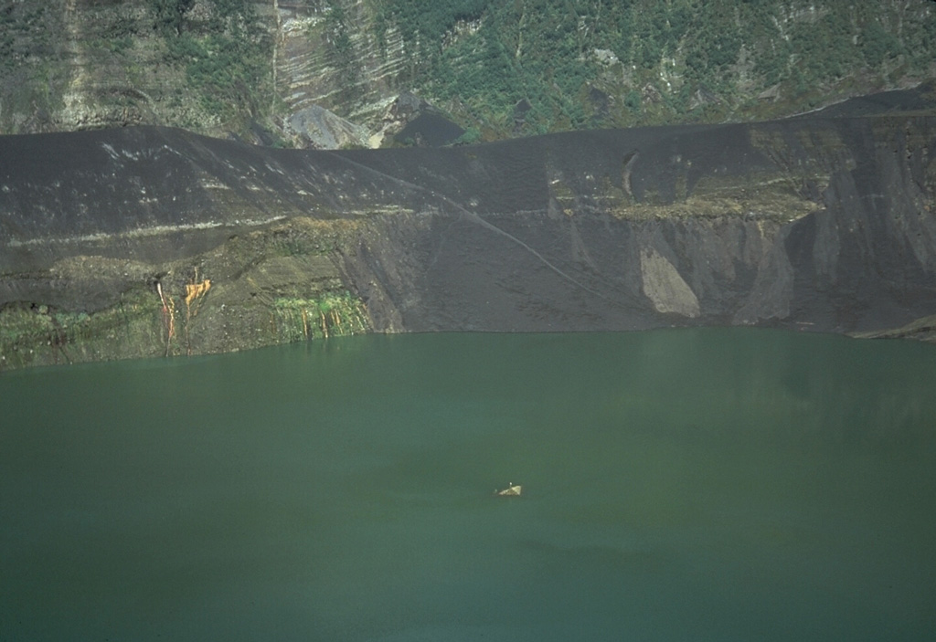 This 28 August 1986 photo from the SE rim of Warirang crater shows the small tip of the January 1983 scoria cone in the center of the lake, just before the cone was completely covered by rising lake waters. Black scoria from the 1982-83 eruption caps the rim of the crater.  Photo by Tom Casadevall, 1986 (U.S. Geological Survey).