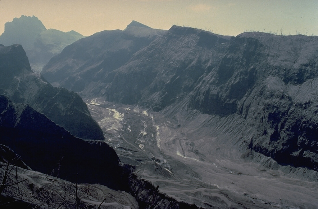 The upper flanks of Kelud volcano were swept by pyroclastic flows during the February 1990 eruption, completely devegetating the slopes of the volcano.  Steam rises from still-hot pyroclastic-flow deposits on the valley floor. Copyrighted photo by Katia and Maurice Krafft, 1990.