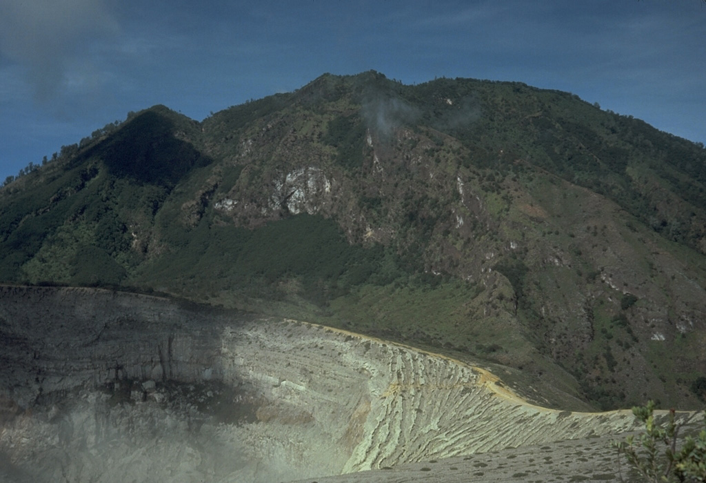Kawah Ijen crater in the foreground is constructed on the flank of Gunung Merapi, the highest peak of the Ijen volcanic complex. Gunung Merapi, less known than the Merapi volcano of central Java, was constructed on the eastern rim of Ijen caldera. Photo by Tom Casadevall, 1987 (U.S. Geological Survey).