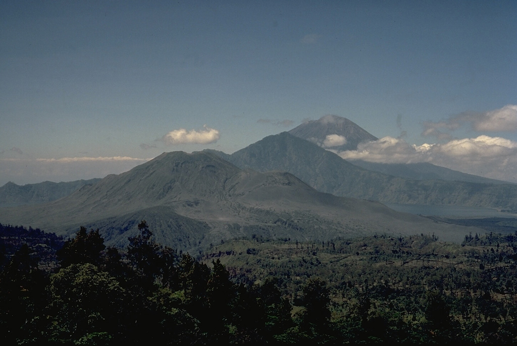 This view from the NW rim of the massive 10 x 13 km outer caldera of Batur volcano looks across the caldera to Gunung Abang (center) on the SE caldera rim.  Lake Batur (right) banks against the SE wall of the outer caldera and overlies the rim of the 7.5-km-wide inner caldera.  Historically active Gunung Batur stratovolcano (left-center) was constructed along a NE-SW-trending line in the center of the inner caldera of Batur volcano.  The large stratovolcano in the distance is Gunung Agung, Bali's highest volcano. Copyrighted photo by Katia and Maurice Krafft, 1971.