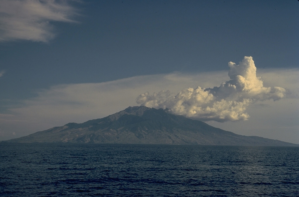 Cumulus clouds drift from the summit of the 13-km-wide island of Sangeang Api off the NE coast of Sumbawa.  Sangeang Api volcano contains two large cones, Doro Api and Doro Montoi.  Intermittent eruptions have been recorded since 1512. Copyrighted photo by Katia and Maurice Krafft, 1971.