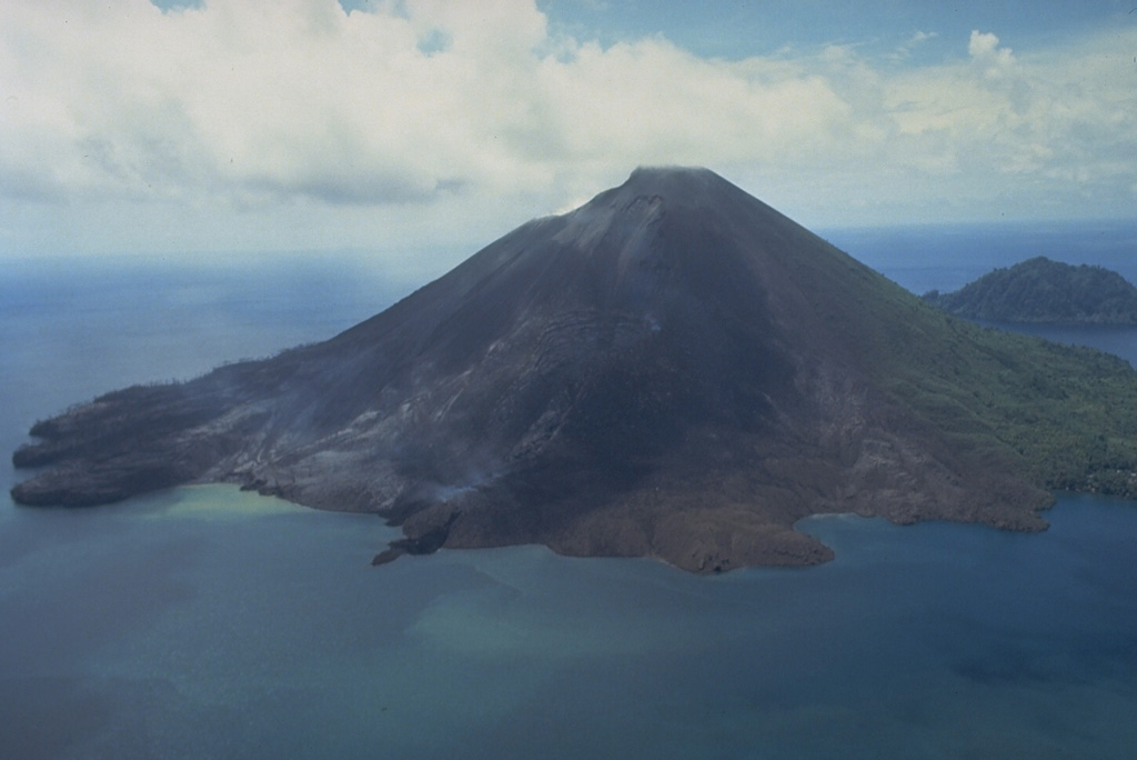 The 640-m-high symmetrical volcano of Banda Api, the most active of a chain of volcanoes in Indonesia's Banda Sea, forms a small 3-km-wide island within a largely submerged 7-km-wide caldera.  This May 19, 1988, view from the south shows vegetation damage from the 1988 eruption and the southern half of a prominent arcuate fissure that extended from the south coast through the summit to 200 m above the north coast.  The still-steaming narrow black lava flow entering the sea to the left of center is one of four erupted in 1988. Photo by Tom Casadevall, 1988 (U.S. Geological Survey).