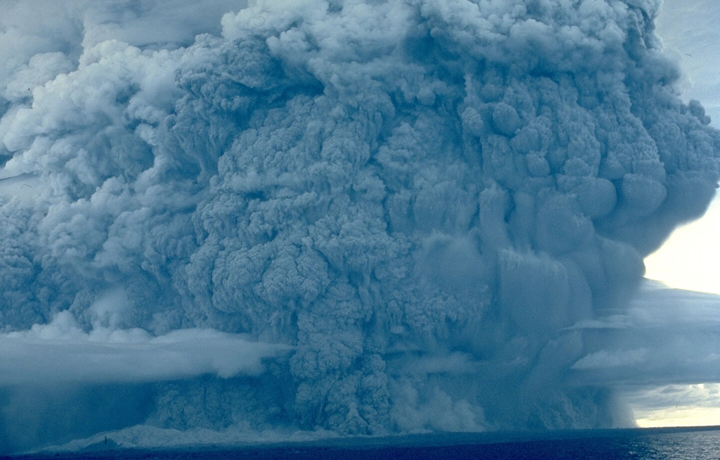 A powerful eruption column rises above Colo volcano on August 22, 1983, and pyroclastic flows sweep to the coast on almost all sides of the island.  The eruption began on July 18; on July 23, the day after evacuation of the island's 7000 inhabitants had been completed, paroxysmal eruptions similar to the one above devastated the island.  Copyrighted photo by Katia and Maurice Krafft, 1983.