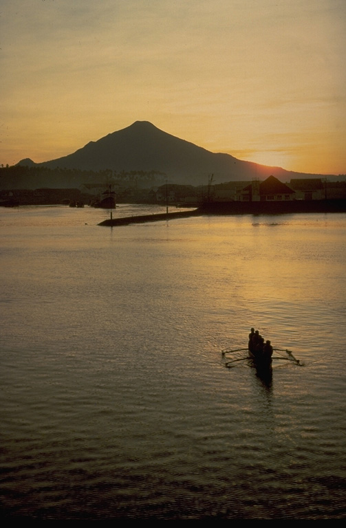 Symmetrical Klabat volcano is silhouetted at sunset above a bay on the NE tip of Sulawesi Island.  The 1995-m-high stratovolcano is the highest of a chain of volcanoes extending along the northern arm of Sulawesi. Copyrighted photo by Katia and Maurice Krafft, 1971.