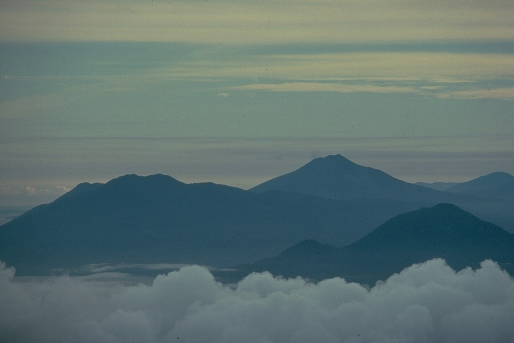 Three Halmahera Island volcanoes are visible in this view from the SW at the summit of Gamalama volcano on Ternate Island.  The twin caldera complex of Todoku-Ranu is on the left, the historically active volcano of Gamkonora is on the skyline at the right center, and Jailolo volcano rises above the clouds at the lower right.  These volcanoes are part of a N-S chain extending along the western coast of northern Halmahera Island. Copyrighted photo by Katia and Maurice Krafft, 1976.