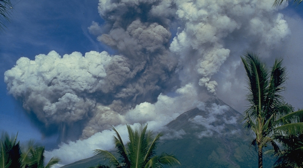 A light-colored plume rises above the summit of Mayon volcano on 14 September 1984, seen here from Cagsawa on the SSE flank. The darker and denser column to its left is an ash plume rising from the pyroclastic flow moving down the SW flank. Photo by Ernesto Corpuz, 1984 (Philippine Institute of Volcanology and Seismology).
