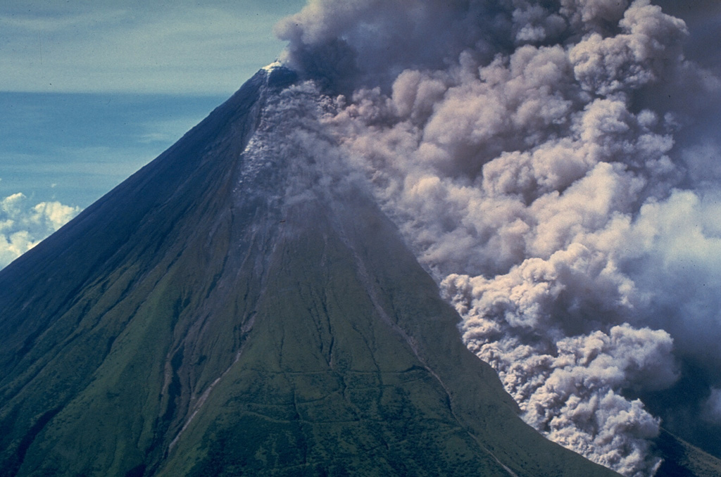 An ash plume rises above a pyroclastic flow traveling down the Buang valley on the upper NW flank of Mayon volcano in the Philippines on 12 September 1984. The front of the advancing pyroclastic flow is visible at the lower right. These pyroclastic flows traveled down to 100 m elevation at rates of about 20 m/s. Photo by Olimpio Pena, 1984 (Philippine Institute of Volcanology and Seismology).