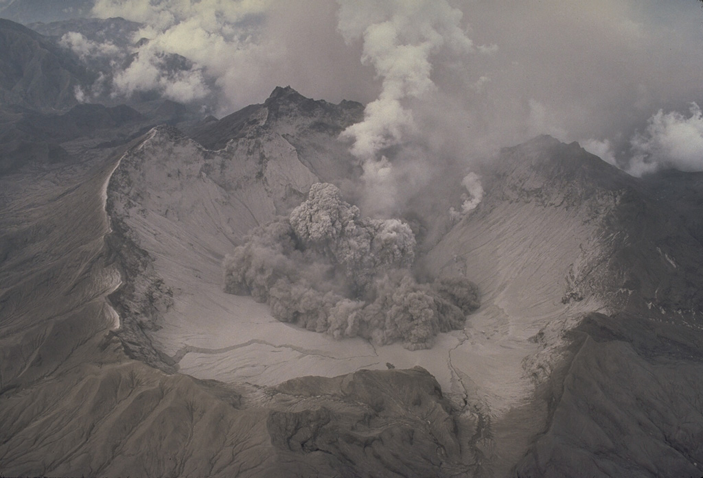 The beginning of a small explosion within the new summit caldera of Pinatubo is seen from the NE on 1 August 1991. After the 2.5-km-wide caldera formed during the 15 June climactic eruption, frequent ash emission lasted through much of July. The caldera floor became visible for the first time when activity changed to intermittent explosions. By September 1991 a lake began to form from the accumulation of rainwater and groundwater from within the volcano; it eventually expanded to cover the caldera floor. Photo by Tom Casadevall, 1991 (U.S. Geological Survey).
