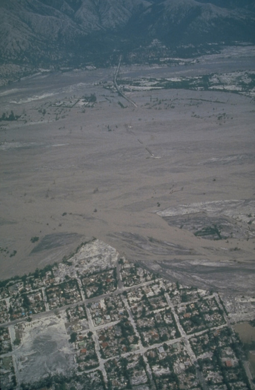 Lahars from Pinatubo fill the broad Santo Tomás River valley SW of the volcano. Erosion along the south bank of the river has cut into the town of San Rafael. This photo was taken a month after the end of the 1991 eruption. Lahars produced by the redistribution of thick deposits of ashfall and pyroclastic flows caused extensive long-term economic devastation which continued for years after the eruption ended. Photo by Chris Newhall, 1991 (U.S. Geological Survey).