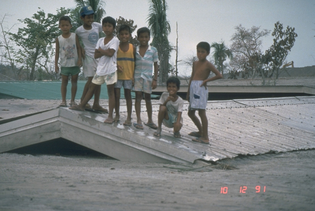 Children stand on top of a school building buried to its roof on 12 October 1991. The school was initially partially buried by lahars from Pinatubo along the Bambam River on 24 August. Successive lahars along this NE-flank valley had traveled 50 km by the end of 1991. Photo by Chris Newhall, 1991 (U.S. Geological Survey).