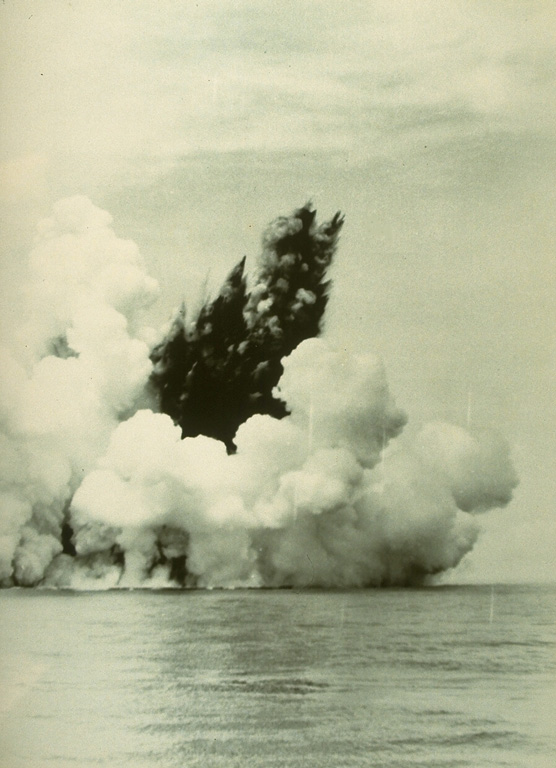 A dark cock’s tail jet is ejected from a submarine vent at Anak Krakatau (Child of Krakatau) on 12 June 1930. A white steam plume rises above a pyroclastic surge that travels along the sea surface in a radial direction from the vent. Base surges such as these are common at submarine eruptions. The first eruptions of Anak Krakatau to breach the surface were seen in December 1927.  Photo by C.E. Stehn, 1930 (courtesy Volcanological Survey of Indonesia).