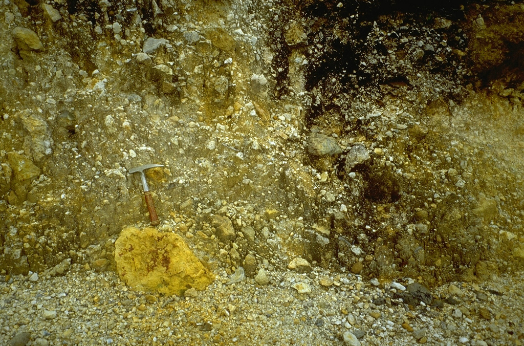 The debris-avalanche deposit produced by the 1772 collapse of Papandayan volcano contains abundant angular clasts including the sulfur-rich clast beneath the rock hammer, in a hydrothermally altered, clay-rich matrix. Extensive thermal alteration of rocks within the volcano had occurred prior to the collapse. Photo by Lee Siebert, 1995 (Smithsonian Institution).