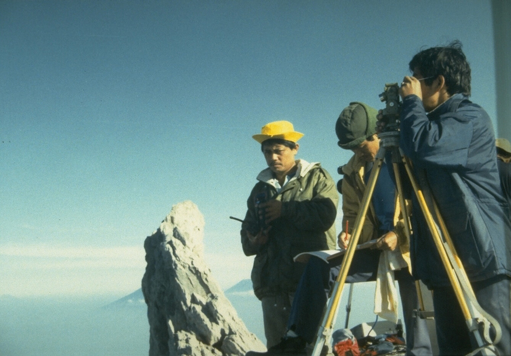 Scientists from the Volcanological Survey of Indonesia make theodolite measurements to determine the height and volume of the growing lava dome at the summit of Merapi volcano in central Java. The pinnacle to the left is the former summit spine of Merapi. Photo by Ruska Hadian, 1993 (Volcanological Survey of Indonesia).