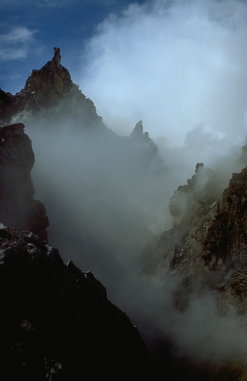 Steam and gas rise between the growing lava dome in the crater of Gunung Merapi and the steep-walled western crater rim (left). The dome visible to the right began growing in 1992. Periodic collapse of the growing dome during successive years produced pyroclastic flows (block-and-ash flows) that devastated the western and southern flanks. Photo by Lee Siebert, 1995 (Smithsonian Institution).