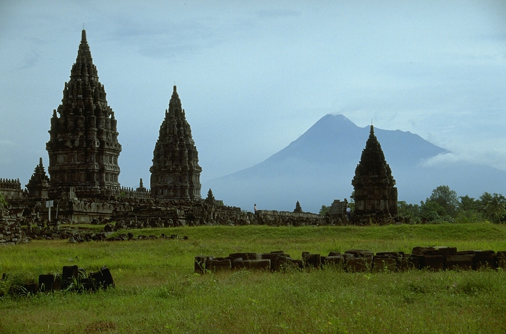 Merapi volcano, one of Indonesia's most active volcanoes, looms above the renowned Hindu temple complex of Prambanan, Indonesia's largest, dating back to 900 CE. Many of the temple complexes on the culturally rich Prambanan plain below Merapi have been affected by lahars (mudflows) that traveled tens of km from the volcano. Photo by Lee Siebert, 1995 (Smithsonian Institution).