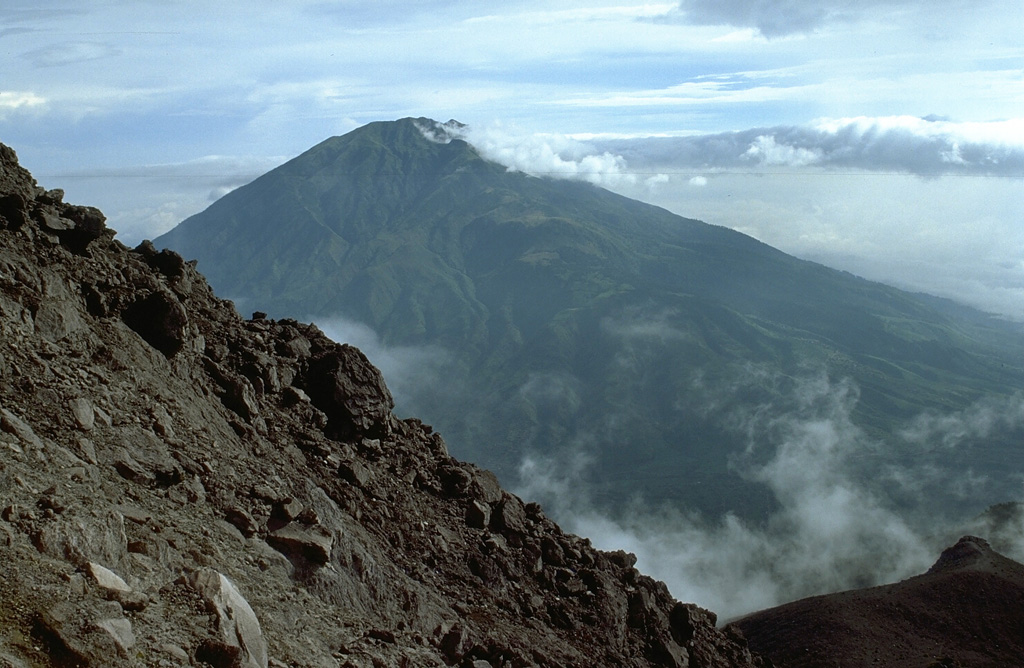 Gunung Merbabu is seen here from the south, near the summit of Merapi. It has prominent radial valleys that extend from the summit of Merbabu towards the NW, NE, and SE. Eruptions have occurred during historical time from Merbabu from the summit crater and from a NNW-SSE fissure system that opened across the summit and fed flank lava flows. Photo by Lee Siebert, 1995 (Smithsonian Institution).