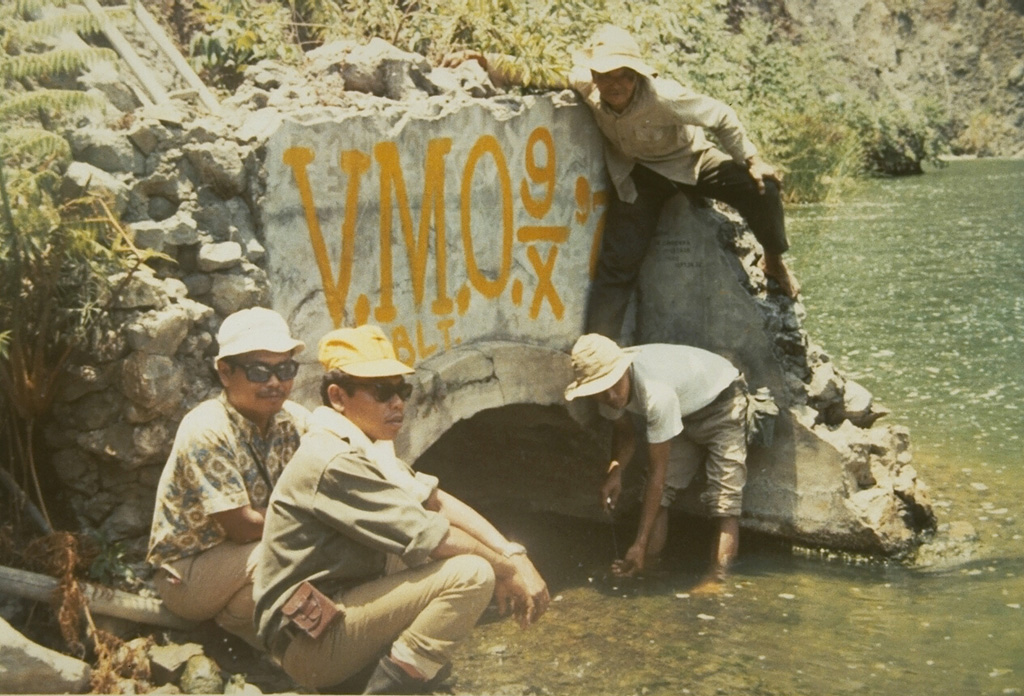 Volcanological Survey of Indonesia scientists measure water levels at a drainage tunnel of Kelud crater lake in 1973. A series of drainage tunnels and shafts were constructed following the devastating 1919 eruption that killed 5,110 people to decrease the amount of water in the summit crater lake. Loss of life from devastating lahars produced by the explosive ejection of crater lake water has been significantly reduced in subsequent eruptions, although a new tunnel needed to be installed after a 1951 eruption deepened the crater by 70 m. Photo by Sumarma Hamidi, 1973 (Volcanological Survey of Indonesia).