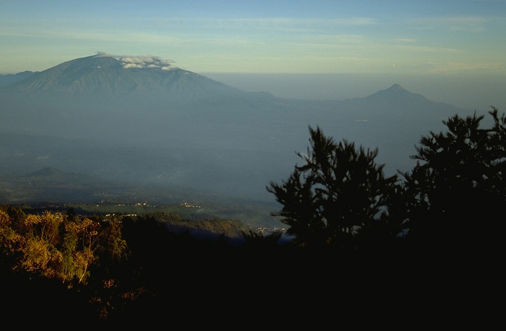 The Arjuno-Welirang volcanic complex (left) and the smaller Gunung Penanggungan volcano (right) are seen here from the SE across a broad valley from the summit of Tengger caldera. A chain of small cones and craters extends across the Arjuno-Welirang complex, while the flanks of the small Penanggungan stratovolcano contain lava flows from flank vents. Photo by Lee Siebert, 1995 (Smithsonian Institution).