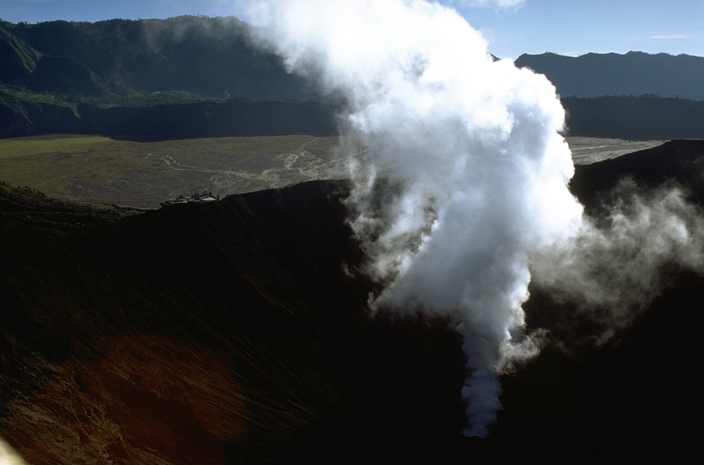 A gas-and-steam plume rises from Bromo crater, one of several post-caldera cones constructed within the Tengger caldera. The low rim of the younger Tengger (Sandsea) caldera rises immediately above the flat caldera floor and the background ridge forms the northern wall of the 16-km-wide Ngadisari caldera. Minor explosive eruptions are common at Bromo, one of Java's most active volcanoes. Photo by Lee Siebert, 1995 (Smithsonian Institution).