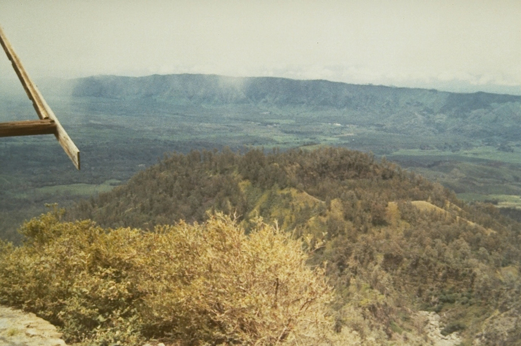 The floor of the 20-km-wide Ijen caldera and its western caldera rim are visible from the rim of Kawah Ijen, a post-caldera cone containing a crater lake. Following formation of the caldera during the Pleistocene, Gunung Merapi was constructed on its eastern rim along with other craters and cones within the southern part of the caldera and along its southern rim. Photo by S. Hamidi, 1973 (Volcanological Survey of Indonesia).