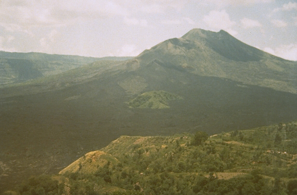 Most of the extensive dark lava flows in the foreground were erupted during 1963-64 from vents near the Batur III cone on the lower SW flank of Batur stratovolcano, viewed here from the village of Penelokan on the southern rim of Batur's outer caldera. The lava flows reached the 7.5-km-wide inner caldera floor and destroyed 16 houses at Tamansari village. Activity has been concentrated along the NE-SW-trending chain of cones and craters. Photo by Sumarma Hamidi, 1973 (Volcanological Survey of Indonesia).