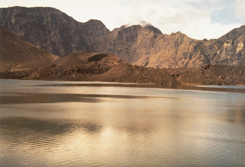 The Rombongan lava dome at the left-center of the photo formed during an eruption in 1944. It was the source of the lava flow that extends to the right (NW) into the Segara Anak caldera lake. Rumblings, ash plumes, and nighttime incandescence began on 25 December 1944. Heavy ashfall took place for 7 days, destroying crops and houses. The Rombongan lava dome was emplaced on the NW flank of Gunung Barujari, whose W flank is visible at the left side of the photo. Photo by Sumarma Hamidi, 1973 (Volcanological Survey of Indonesia).