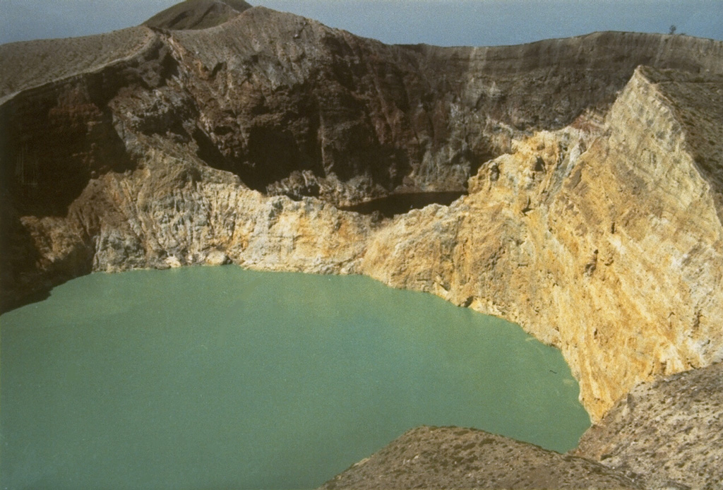 The walls of Tiwu Nua Muri Kooh Tai, the middle of Kelimutu's three crater lakes, expose bedded hydrothermally altered rocks. Tiwu Ata Polo, the darker-colored crater lake to the SE, is visible beyond the far wall. Constant upwelling occurs at these two lakes, probably as a result of subaqueous fumaroles, directing floating sulfur in Tiwu Nua Muri Kooh Tai toward the crater walls. Photo by L.D. Reksowirogo, 1972 (Volcanological Survey of Indonesia).