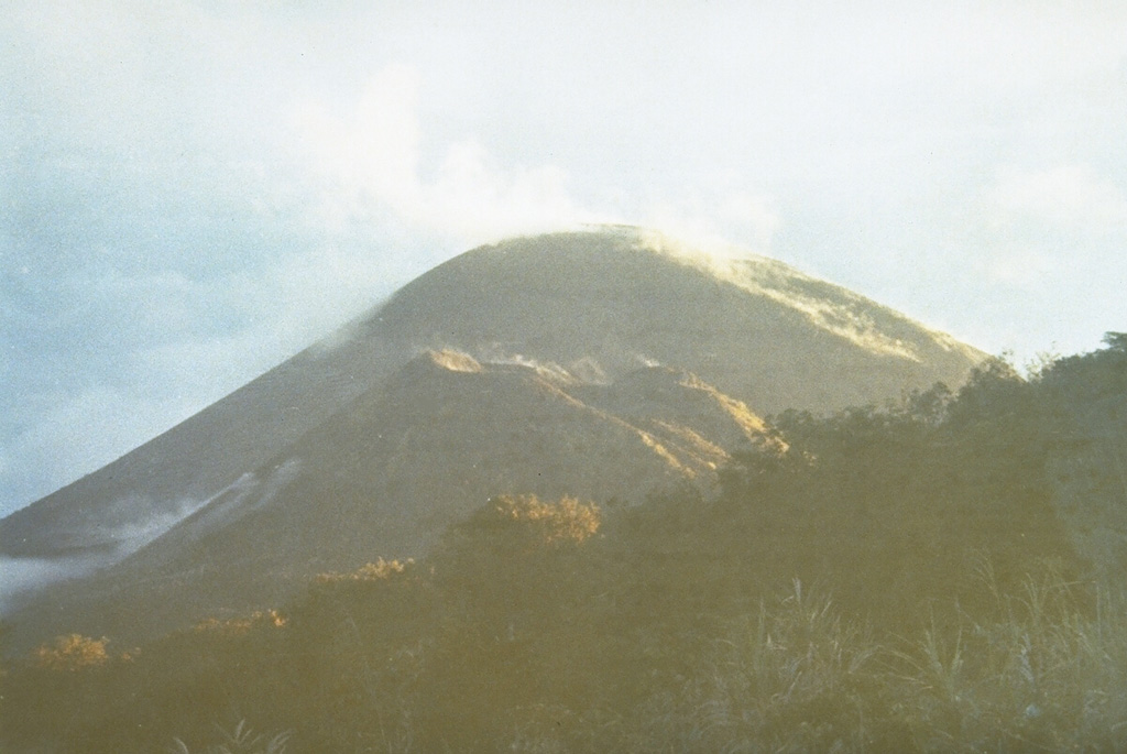 Soputan volcano, a small 580-m-high stratovolcano, seen here from Bukit Keledondei on the NE side, is a youthful, largely unvegetated volcano with a prominent flank cone, Aeseput, visible here in the center of the photo.  Soputan is one of Sulawesi's most active volcanoes; both it and Aeseput, which was formed in 1906, have erupted frequently since the 18th century. Photo by Ruska Hadian, 1973 (Volcanological Survey of Indonesia).