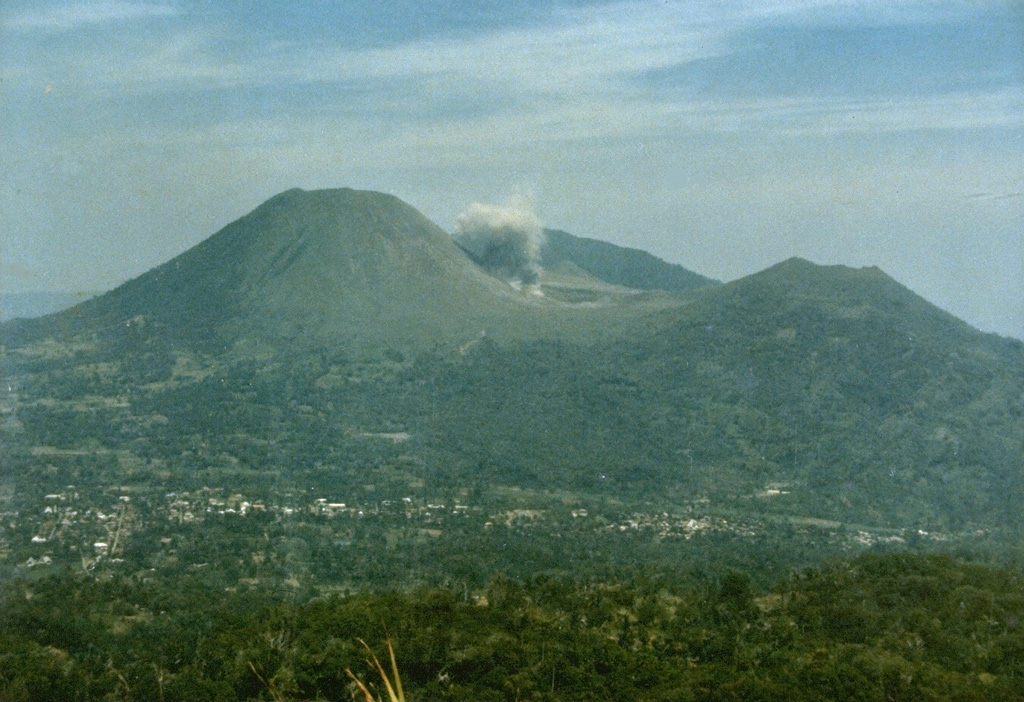 A small ash plume, viewed here from the east on the slopes of Mahawu volcano, rises on September 15, 1986 above Tompaluan crater in the saddle between Lokon and Empung volcanoes.  This was one of many explosions that occurred at Lokon-Empung during an eruption between March 1986 and May 1987.  The peak behind the eruption plume is Gunung Tetawiran, part of a volcanic ridge that extends to the NW from Lokon volcano. Photo by Ruska Hadian, 1986 (Volcanological Survey of Indonesia).