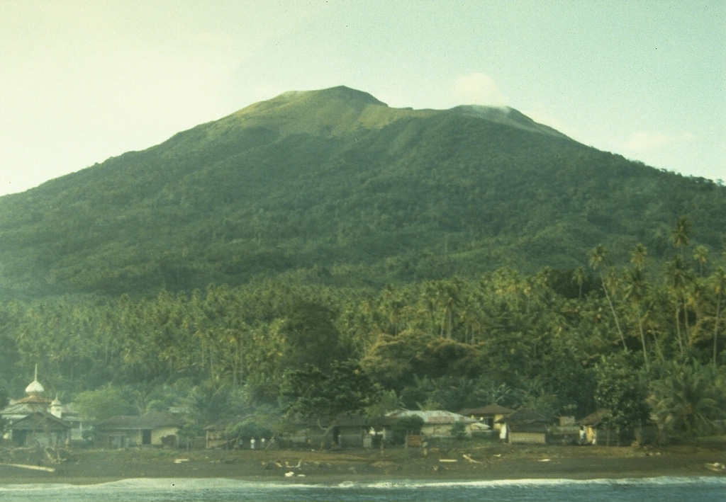 Gamkonora volcano, seen here from the NW coast near Gamsungi village, is one of Halmahera's more active volcanoes.  The summit crater of Gamkonora is elongated in a N-S direction, with a small crater lake at the north end.  The first two historical eruptions, in 1564 or 1565, and in 1693, were the most severe, producing respectively a destructive lava flow that reached the sea, and a tsunami that inundated villages. Photo by A. Solihin, 1984 (Volcanological Survey of Indonesia).