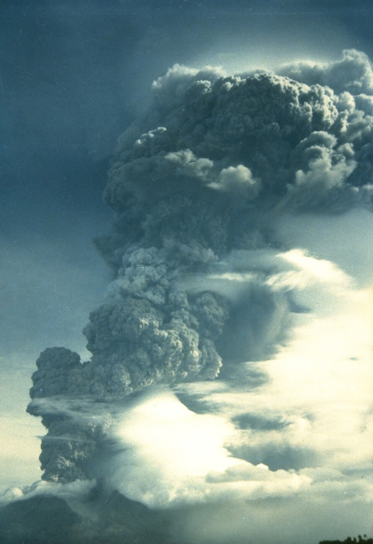 A vigorous eruption column rises above Makian volcano in this 1988 view from neighboring Moti Island.  The six-day eruption began on July 29, producing eruption columns that reached 8-10 km altitude.  Pyroclastic flows on the 30th reached the coast of the island, whose 15,000 residents had been evacuated.  A flat-topped lava dome was extruded in the summit crater at the conclusion of the eruption. Photo by Willem Rohi, 1988 (Volcanological Survey of Indonesia).