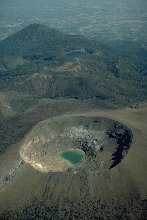 Shinmoe-dake crater in the foreground is one of the most active volcanoes of the Kirishima volcano group.  Historical eruptions have occurred at Shinmoe-dake since the 17 th century.  Hinamori-dake stratovolcano appears to the NE at the upper right, and the Ohata-ike maar to its right is filled by a blue lake. Copyrighted photo by Katia and Maurice Krafft.