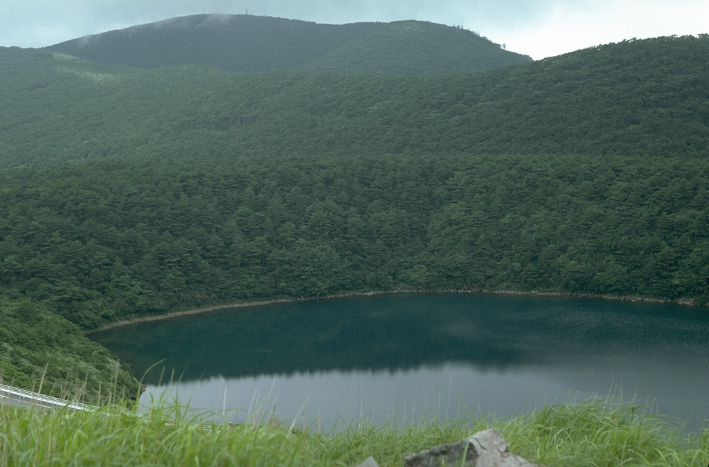 Lake-filled Rokkannon-Miike is one of several maars in the Kirishima volcano group. It is located NW of Karakunidake in the NW part of the group. The forested rim of the maar is across the center of the photo and the peak behind it is Shiratoriyama. Photo by Lee Siebert, 1988 (Smithsonian Institution).
