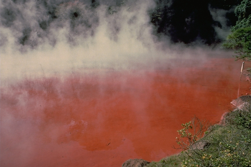 Chino-ike is one of the most colorful of the Jigoku, or "Hells," in the Beppu thermal area of Tsurumi volcano on the Japanese island of Kyushu.  Steam rises above the iron-stained, vermillion hot-spring pool.  Other pools in the Beppu area are milky, light blue, greenish blue, or indigo blue. Copyrighted photo by Katia and Maurice Krafft, 1981.