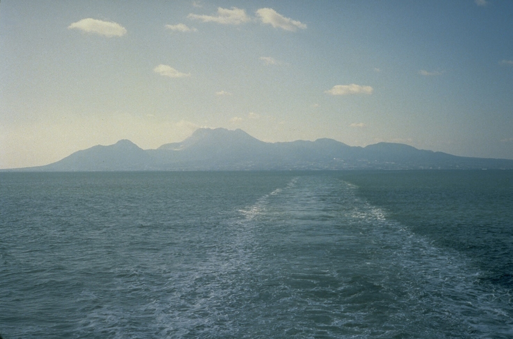 The Unzen volcanic complex comprises much of the Shimabara Peninsula east of Nagasaki, seen here looking to the W from across Shimabara Bay. Three large edifices are visible: Kinugasa to the N, Fugendake in the E-center, and Kusenbu on the S. Historical eruptive activity has occurred at the summit and flanks of Fugendake. Activity during 1990-95 formed a lava dome at the summit that produced pyroclastic flows (block-and-ash flows). Photo by Tom Casadevall, 1991 (U.S. Geological Survey).