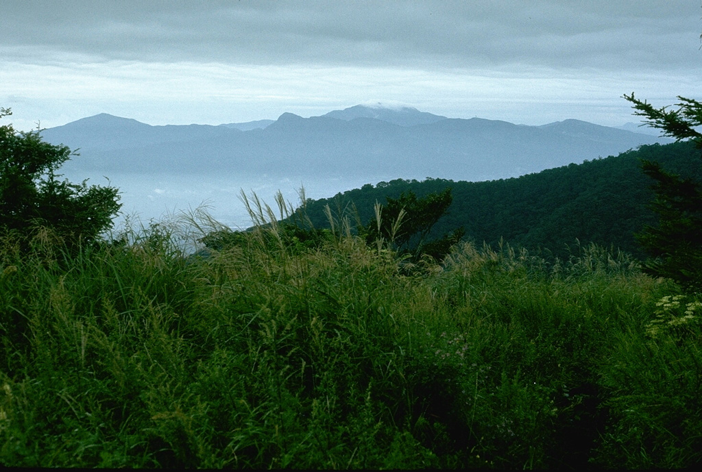 Hakoneyama volcano, seen here from the W, is a broad volcano with two large calderas. A group of lava domes formed in the center of the caldera. The highest dome, Kamiyama, forms the high point of the complex, topped by clouds in the center of the photo. The caldera formed during two large Pleistocene eruptions. An eruption took place around 3,000 years ago and seismic swarms have occurred frequently during the 20th century. Photo by Lee Siebert, 1977 (Smithsonian Institution).