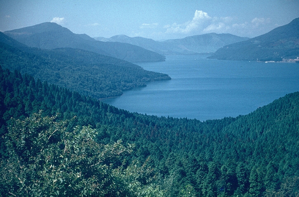 Lake Ashi, seen here from the SE, occupies the SW corner of Hakone caldera. Hakoneyama contains two calderas, the largest of which is 10 x 11 km. The arcuate caldera rim is to the left and the flanks of a group of post-caldera cones form the right-hand shoreline. Post-caldera eruptions have constructed a half dozen lava domes along a SW-NE trend across the center of the calderas. An eruption took place around 3,000 years ago and seismic swarms occurred frequently during the 20th century. Photo by Lee Siebert, 1963 (Smithsonian Institution).