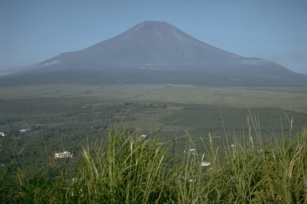 During summer the flanks Mount Fuji have oxidized scoria and lava flows visible above the timberline. The two “shoulders” on the lower flanks, in this view from the north near Lake Yamanaka, are remnants of a group of older volcanoes over which the modern symmetrical volcano was constructed. The shoulder to the left is a remnant of Kofuji (Old Fuji) volcano, and the broader shoulder to the right is a segment of Komitake, a mid-Pleistocene volcano. Photo by Lee Siebert, 1970 (Smithsonian Institution).