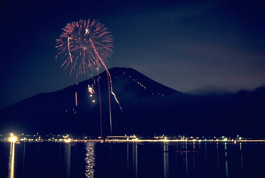 Mount Fuji is a popular tourist destination, seen here providing the backdrop to a fireworks display at Lake Yamanaka, one of five lakes at the northern base of the volcano. The line of diagonal lights extending up the right-hand side of Fuji are mountain huts along the ten stations of the Fuji-Yoshida climbing route, the most popular of the six major summer ascent routes. Photo by Lee Siebert, 1963 (Smithsonian Institution).