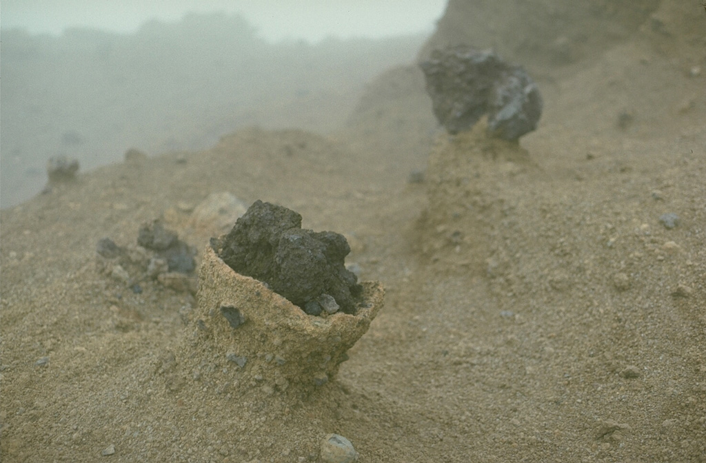 Volcanic bombs ejected during the eruption of Mount Fuji in 1707 within light-colored tephra from the older Kofuji edifice. These blocks, about 30 cm in diameter, impacted the surface of the older tephra deposits near the rim of the 1707 Hoei crater. Erosion by strong winds removed the softer, hydrothermally altered tephra, leaving the blocks above the surface. Photo by Lee Siebert, 1977 (Smithsonian Institution).