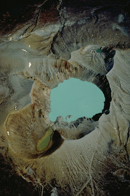 A near-vertical 1981 aerial photo looks down on the summit craters of Kusatsu-Shirane volcano, with NE at the top of the photo.  Three partially overlapping craters form the summit.  Kara-gama is at the bottom, the lake-filled Yu-gama at the center, and Mizu-gama at the top.  Eruptions, mostly consisting of small-to-moderate phreatic explosions, have occurred from all three craters during historical time, with Yu-gama being the most active.  Prior to an eruption in 1882, Mizu-gama and Yu-gama contained clear lakes with vegetated shores. Copyrighted photo by Katia and Maurice Krafft, 1981.