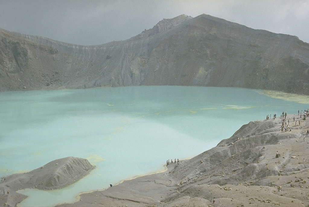 The summit of Kusatsu-Shiranesan contains three craters with the largest, Yugama, holding the turquoise lake shown here. Rafts of yellow sulfur float on the surface of the acidic lake. This 1977 view looks across the lake from the SW-most crater (Karagama) to the NE-most crater (Mizugama), located beyond the notch to the left. Small-to-moderate phreatic explosions have been recorded from all three craters since the 1800s. Photo by Lee Siebert, 1977 (Smithsonian Institution).