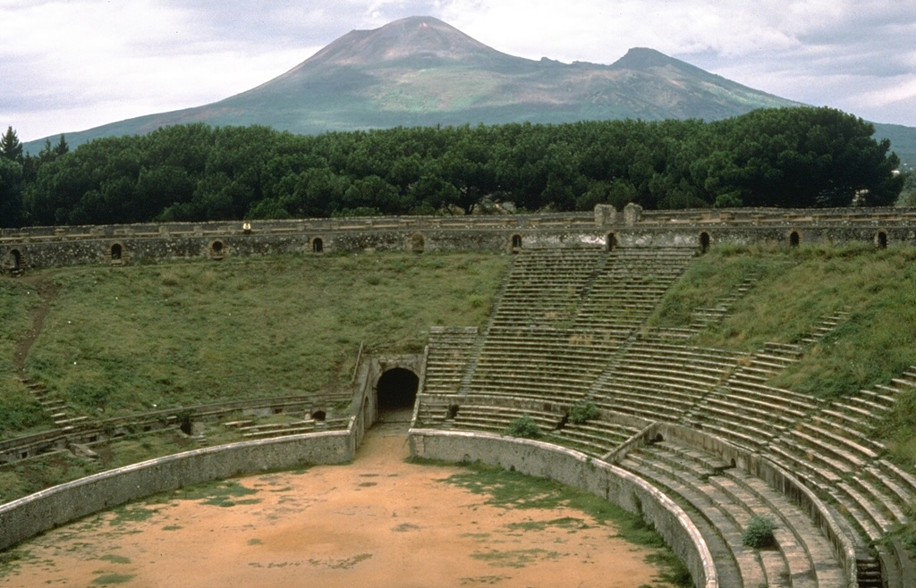 Vesuvius rises above an excavated stadium in the buried city of Pompeii. The 79 CE eruption began on 24 August with phreatomagmatic explosions that produced widespread ashfall. Many residents of Pompei and other towns had evacuated prior to the onset of devastating pyroclastic flows the following day that swept over broad areas as far as 30 km from the volcano and caused several thousand fatalities. Photo by Dan Dzurisin (U.S. Geological Survey), 1983.