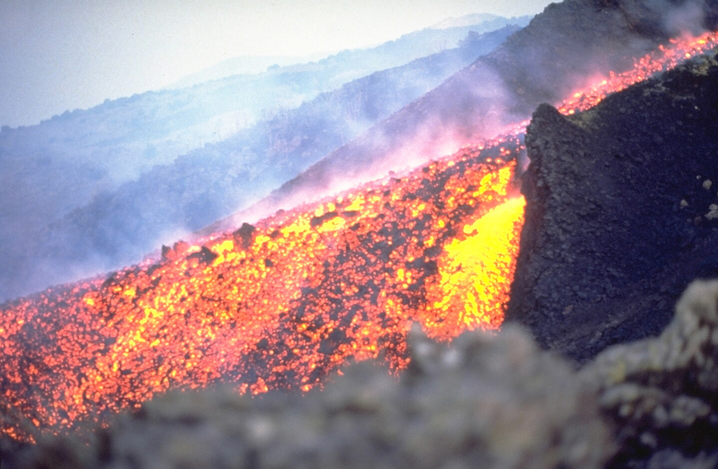 An active lava channel near the vent of the March 1981 NW flank eruption fed flows that traveled 7.5 km. The week-long eruption, one of few Etna eruptions originating on the NW or NNW flanks, entered populated areas and resulted in evacuations. Active vents progressively migrated downhill along eruptive fissures between 2,250 and 1,150 m altitude and produced vigorous lava fountains and lava flows. Photo by Roberto Scandone (University of Rome).