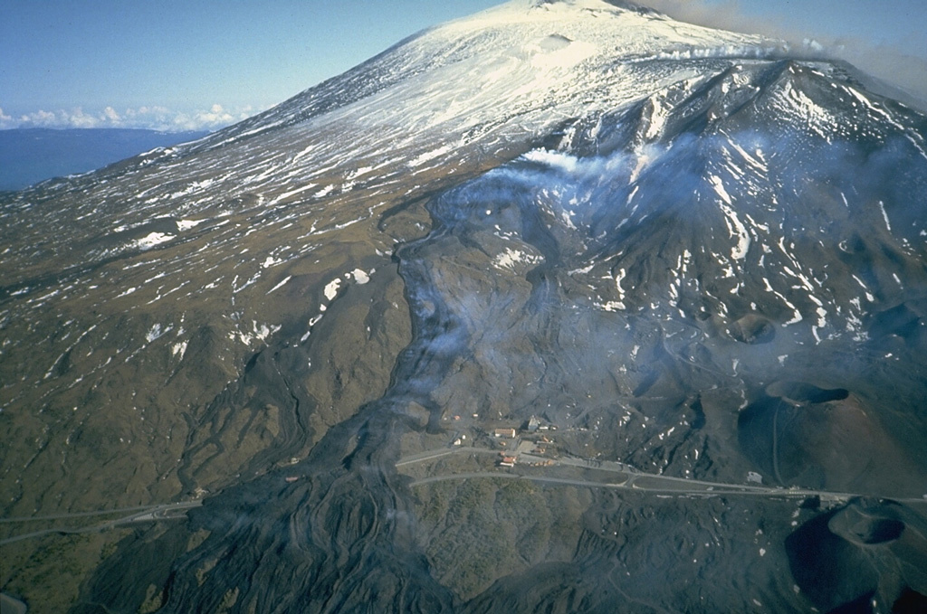 Black lava flows descend the south flank of Etna a week after the eruption began on 28 March 1983 and went on to last for five months. Prominent levees are visible on the surface of the lava flows that crossed a highway and formed a complex lava field as much as 1 km wide. The flows originated from a NNE-SSW-trending fissure 4 km S of Etna's snow-capped Central Crater. Photo by Romolo Romano, 1983 (IIV-CNR, Catania, Italy).