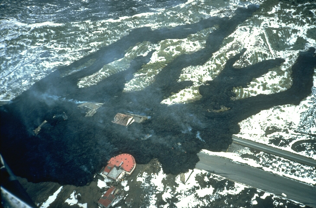 Fresh black lava flows overrun a highway and tourist facility buildings the day after the start of an eruption at Sicily's Mount Etna on 28 March 1983. The lava flows originated from a fissure 4 km S of the summit, and over a 5-month period formed a complex lava field as much as 1 km wide. Photo by Romolo Romano, 1983 (IIV-CNR, Catania, Italy).