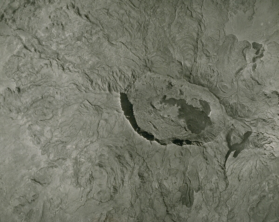 A vertical aerial photo of the Quaternary Fentale volcanic complex, lying along the main Ethiopian rift zone, has a prominent summit caldera and lava flows along its flanks. The 3 x 4 km caldera with steep-sided walls up to 500 m high is elongated perpendicular to the direction of the regional fissures of the Ethiopian Rift. Note the recent rhyolitic obsidian lava flow to the NE (upper right) marked with curved flow ridges. The dark lava flow on the caldera floor was erupted in 1820. Photo by Imperial Highway Authority of Ethiopia (published in Green and Short, 1971).